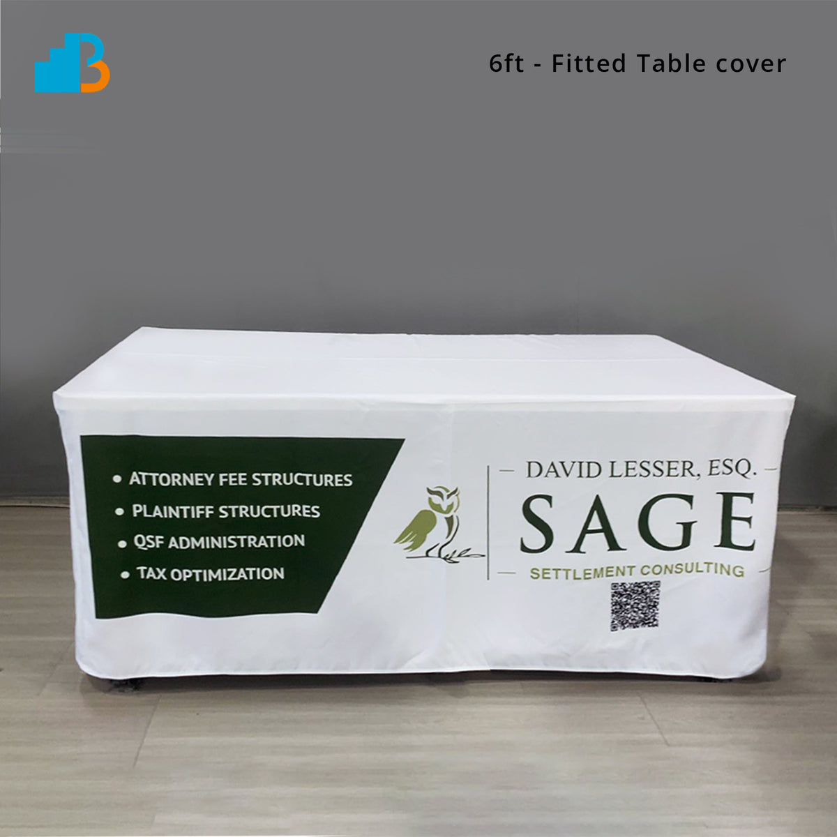A white fitted table cover draped over a rectangular table, printed. The photo is taken in an indoor room with gray walls and light wood flooring, with text in the top right reading '6ft - Fitted Table cover'.
